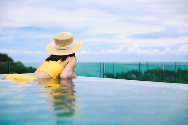 Mulher asiática com chapéu e biquíni relaxa em resort com piscina infinita em Phuket, Tailândia