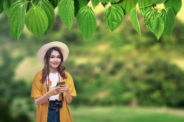 Mulher asiática com chapéu e câmera segurando um celular viajando