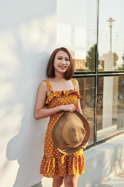 Mulher asiática com chapéu e vestido vintage em pé junto à parede