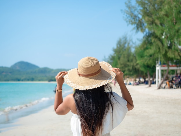 Mulher asiática com chapéu fofo na praia com oceano azul e céu com fundo de viagens de pessoas de turismo