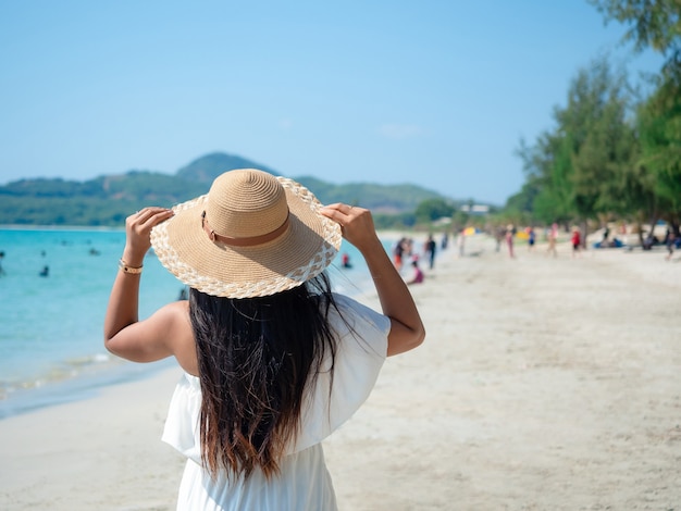 Mulher asiática com chapéu fofo na praia com oceano azul e céu com fundo de viagens de pessoas de turismo