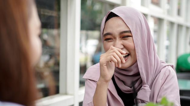 Mulher asiática com hijab sorrindo em um café com uma amiga