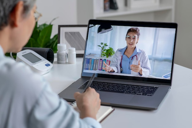 Mulher asiática com laptop durante uma consulta on-line com seu médico em seu conceito de telemedicina na sala de estar