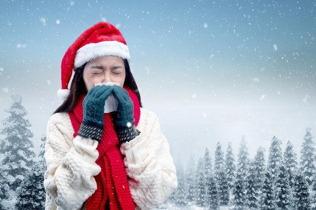 Mulher asiática com luvas de inverno e chapéu de Papai Noel pega gripe espirros no campo de neve