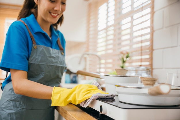 Mulher asiática com luvas de proteção limpando fogão de gás na cozinha Enfatizando a higiene limpando a mão do pó com um pano Limpador no trabalho luva de segurança limpeza de casa rotina empregada doméstica conceito de limpeza doméstica