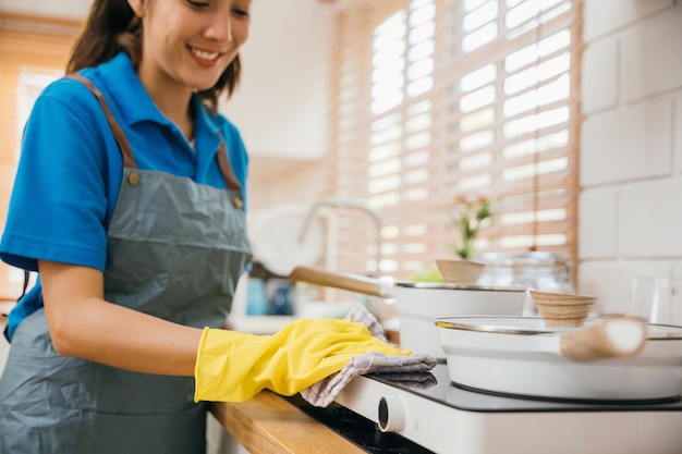 Mulher asiática com luvas de proteção limpando fogão de gás na cozinha Enfatizando a higiene limpando a mão do pó com um pano Limpador no trabalho luva de segurança limpeza de casa rotina empregada doméstica conceito de limpeza doméstica