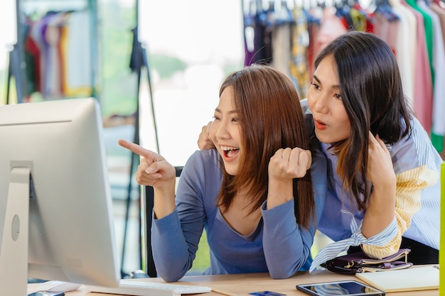 Mulher asiática com mão emocionante do amigo apontando para a tela do computador para o conceito de proprietário de empresa jovem feliz.