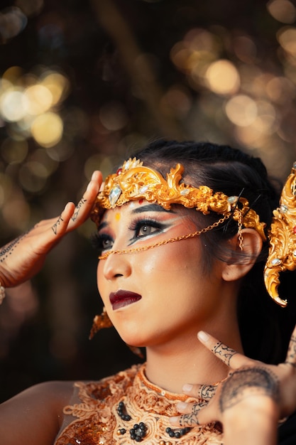 Mulher asiática com maquiagem cobrindo o rosto com a mão enquanto se maquiava e usava uma coroa de ouro e uma tiara de ouro