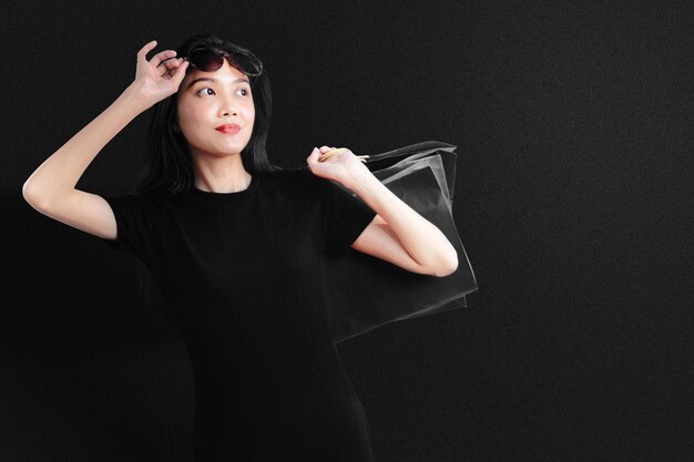 Mulher asiática com óculos de sol, carregando uma sacola de compras com um fundo preto. conceito de black friday