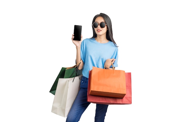 Mulher asiática com óculos escuros carregando sacolas de compras segurando o celular isolado sobre fundo branco