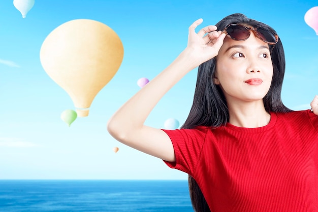 Mulher asiática com óculos escuros e balão de ar colorido voando com fundo de céu azul