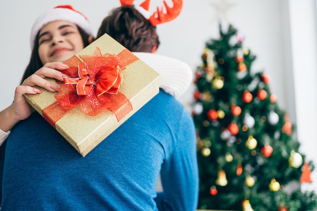 Mulher asiática com presente surpresa de natal abraçando marido em casa apresentando presente como tradição de véspera de natal comemorando ano novo mulher asiática feliz recebendo parabéns de seu namorado