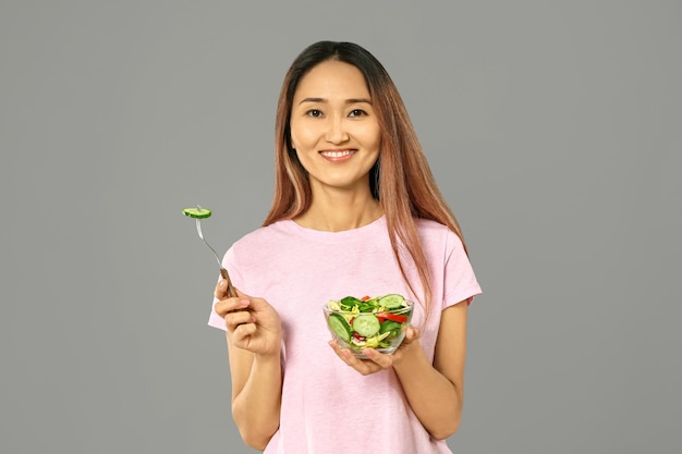 Mulher asiática com salada de legumes em fundo cinza