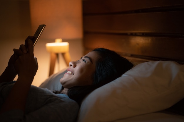 Mulher asiática com telefone inteligente enquanto deitado na cama