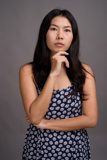 Mulher asiática com vestido azul contra parede cinza