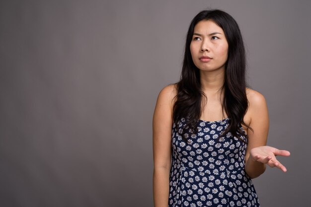 Mulher asiática com vestido azul contra parede cinza