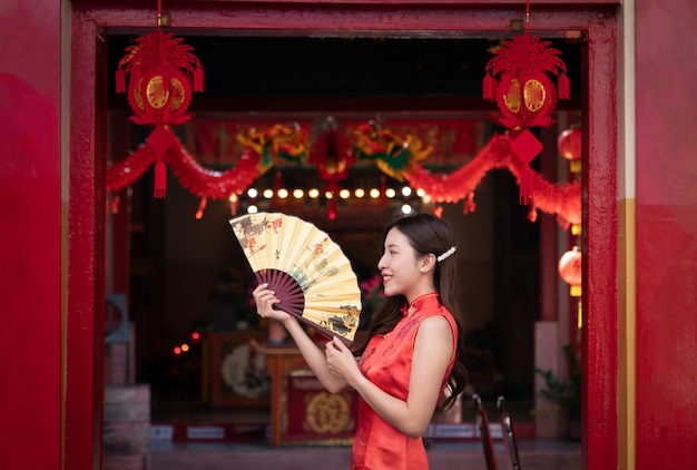 Mulher asiática com vestido Cheongsam vermelho e segurando um leque de ouro no santuário chinês. Conceito de ano novo chinês.