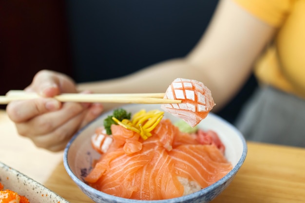 Mulher asiática comendo fatia de sashimi de salmão com arroz em restaurante japonês