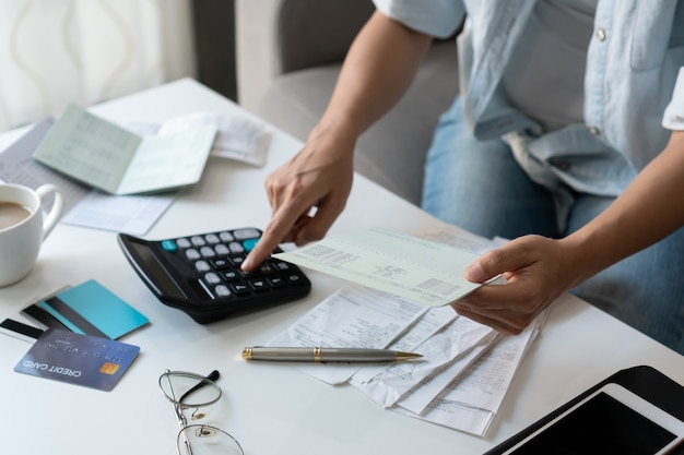 Mulher asiática consideravelmente nova que usa a calculadora ao guardar o livro de conta bancária para calcular despesas e impostos home na sala de visitas em casa.