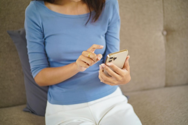 Mulher asiática controlando telefone celular doméstico inteligente com aplicativo doméstico inteligente na tecnologia de tela sensível ao toque da sala de estar Sistema de controle doméstico remoto
