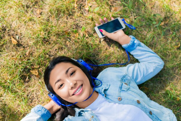 Mulher asiática curtindo a música enquanto estava deitada na grama no parque da cidade