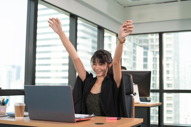 Mulher asiática de beleza levantando as duas mãos depois de terminar o trabalho sorrindo feliz olhando a tela do laptop