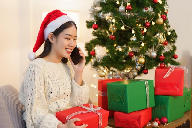 Mulher asiática de conceito de natal sentada na sala de estar decorada de natal e falando no smartphone