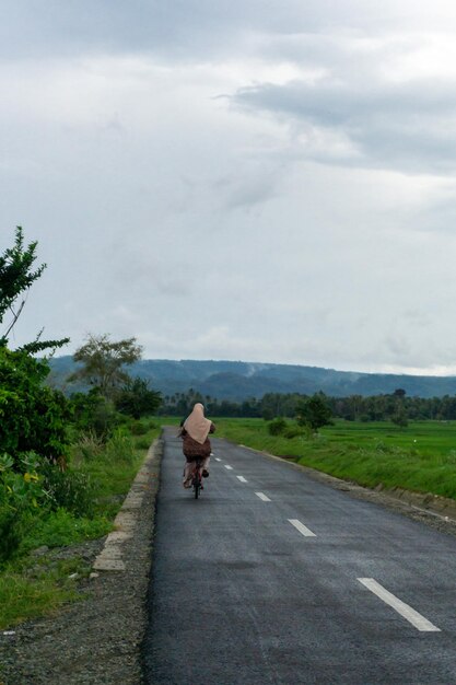 Mulher asiática de hijab andando de bicicleta pela manhã na estrada de asfalto Uma menina andando de ciclismo com uma montanha