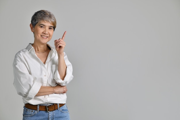 Mulher asiática de meia idade apontando os dedos para o espaço vazio da cópia para o texto isolado no fundo branco