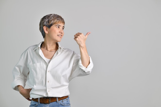 Mulher asiática de meia idade apontando os dedos para o espaço vazio da cópia para o texto isolado no fundo branco