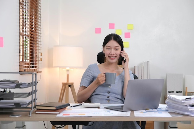 Mulher asiática de negócios usando smartphone para fazer finanças matemáticas na mesa de madeira no conceito financeiro de contabilidade fiscal de escritório