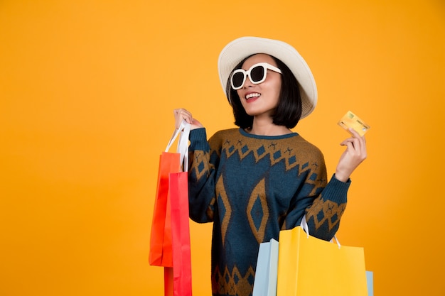 Mulher asiática de óculos, segurando sacos de papel coloridos e um cartão de crédito