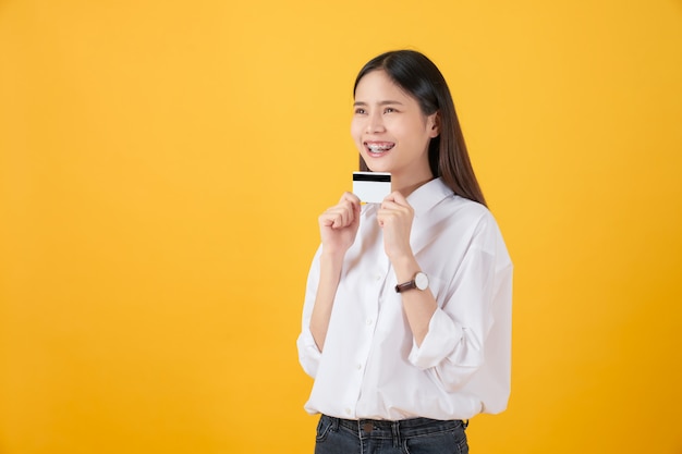 Mulher asiática de sorriso que guarda o pagamento com cartão de crédito no fundo amarelo com espaço da cópia.