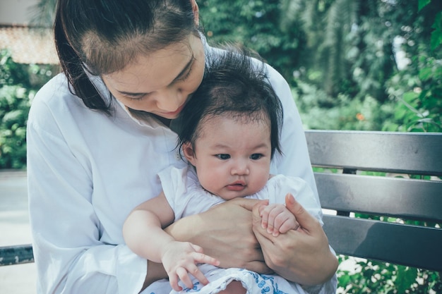 Mulher asiática de vestido branco e seu bebê brincando de felicidade no parque conceito de dia das mães ao ar livre