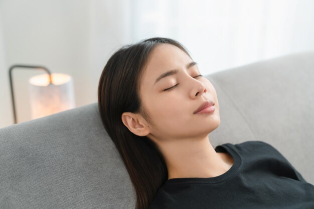 Mulher asiática descansando confortavelmente e relaxando em um sofá depois do trabalho em casa