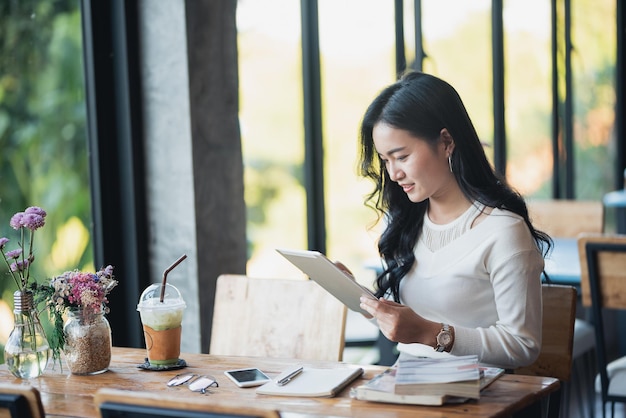 Mulher asiática digitando mensagem de texto no tablet em um café jovem mulher asiática sentada em uma mesa com um café usando o mercado de ações de negociação de tablet ou moeda criptográfica