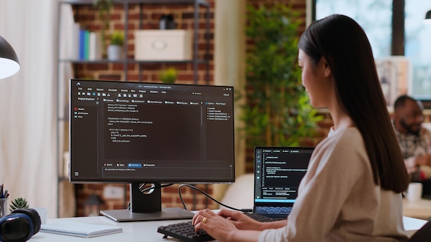 Mulher asiática é vista digitando código para um projeto de desenvolvimento de aplicativo em seu computador