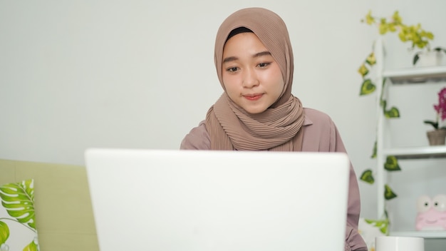 Mulher asiática em hijab olhando para a tela do laptop em casa