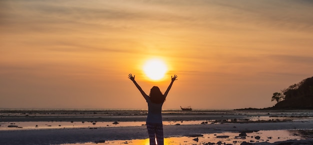 Foto mulher asiática em pé na praia à beira-mar no céu da manhã com fundo do nascer do sol.