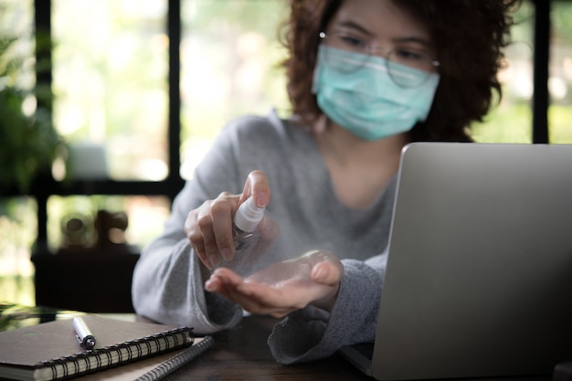 Foto mulher asiática em quarentena e distanciamento social usando máscara cirúrgica e limpando as mãos com desinfetante em gel de álcool enquanto trabalhava em casa durante a pandemia de coronavírus covid-19