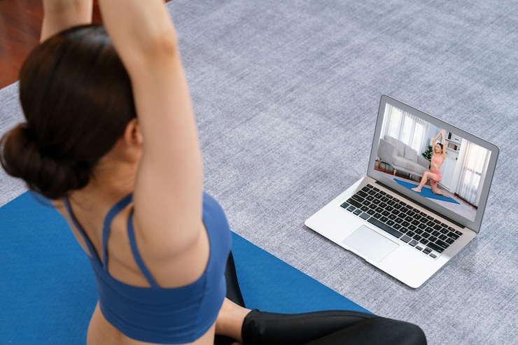 Foto mulher asiática em roupas esportivas fazendo exercícios de ioga no tapete de fitness como sua rotina de treinamento em casa, cuidados com o corpo saudável, estilo de vida, mulher assistindo vídeo de ioga on-line no laptop vigoroso