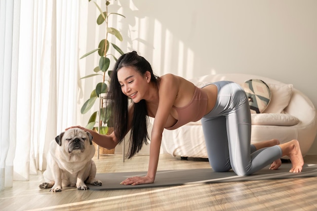 Mulher asiática em roupas esportivas se exercitando e fazendo ioga com um cão bonito na sala de estar em casa