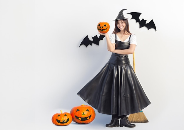 Foto mulher asiática em traje de bruxa mostrando cabeça de abóbora de halloween e fundo de decoração no festival de halloween