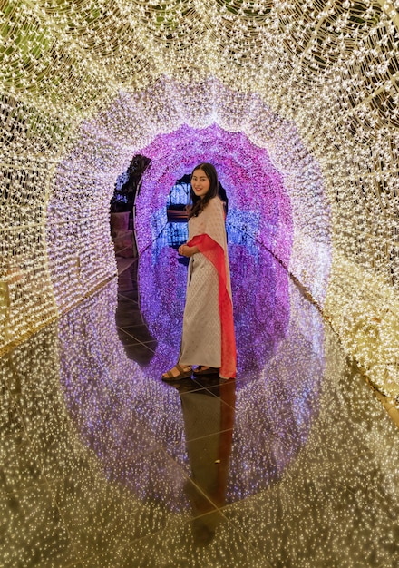 Mulher asiática em traje tradicional tailandês em pé com túnel de iluminação colorido iluminado com reflexo no chão
