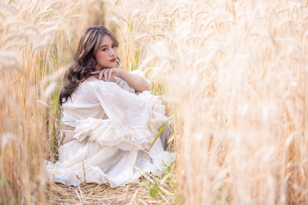 Mulher asiática em um campo de trigo Retrato de mulher bonita em campo de trigo sorrindo Mulheres bonitas asiáticas em vestido branco caminhando campos de cevada dourada