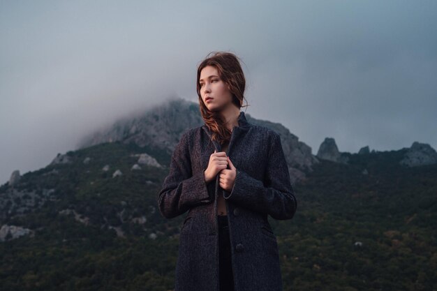 Mulher asiática em um casaco cinza, apreciando a vista nas montanhas