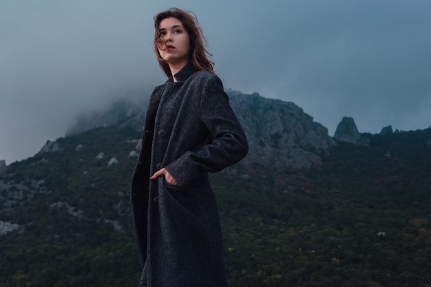 Mulher asiática em um casaco cinza, apreciando a vista nas montanhas