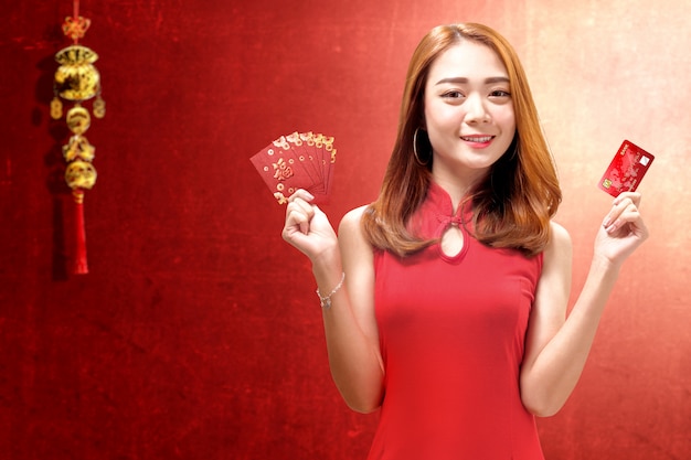 Mulher asiática em um vestido cheongsam segurando um cartão de crédito e envelopes vermelhos