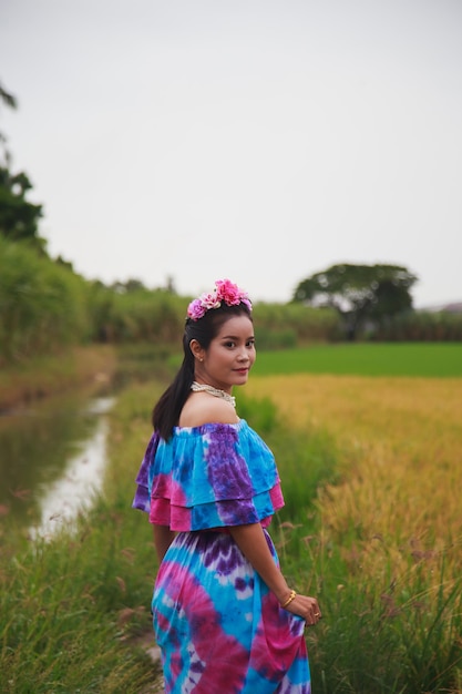 Mulher asiática em um vestido de cor estampada em frente a um campo de arroz