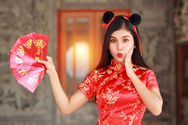 Mulher asiática em vestido chinês vermelho tradicional cheongsam qipao com gesto de mostrar um envelope vermelho com emoção emocionante